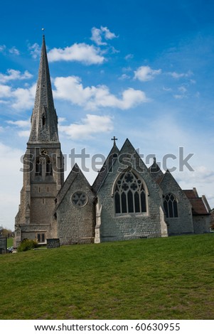 All Saints Parish Church, Blackheath, London, against blue sky with white clouds and green grass lawn in the foreground