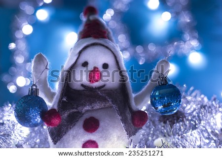 Snowman smiling brought Christmas balls, turquoise background with flashing lights