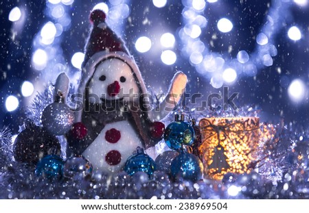 Snowman smiling brought Christmas balls, blue background with flashing lights snowing