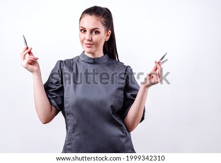 Brunette shows eyebrow tweezers in hands. Girl beautician with tool in hands. White background in studio Foto stock © 