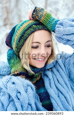 Young woman winter portrait. Happy blonde girl in the winter park wearing winter gloves covered with snow flakes. Christmas snowing portrait concept.