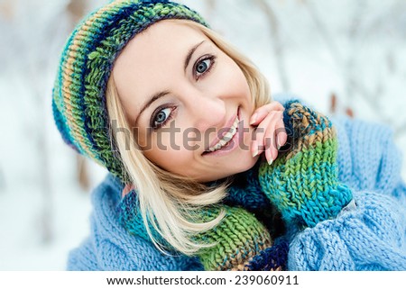 Winter portrait of beautiful blonde woman smiling. Winter park with snow. Bright smile and colorful wear. Blue clothes.