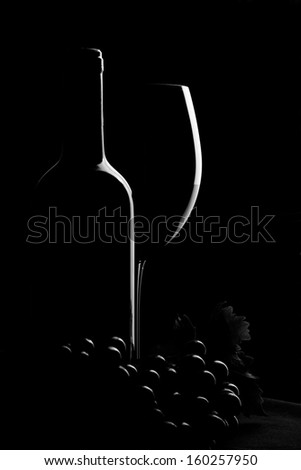 Wine Concept. Bottle of wine with glass and grapes on white desk over black background.