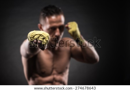 Muscular young man in boxing gloves and shorts shows the different movements and strikes in the studio on a dark background
