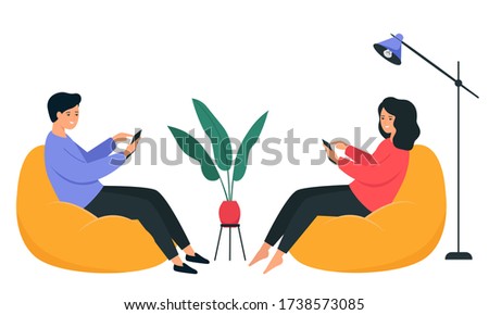 A guy and a girl are sitting on a bean bag chair and holding a smartphone in their hands. Happy young people communicate on the Internet. 