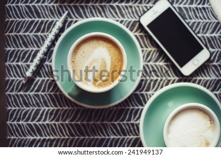 Fresh cup of cappuccino in a green cup on a coffee table with a smartphone and a notebook