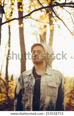 man half took off his rubber bird mask, standing in the autumn sunset forest thinking dramatically
