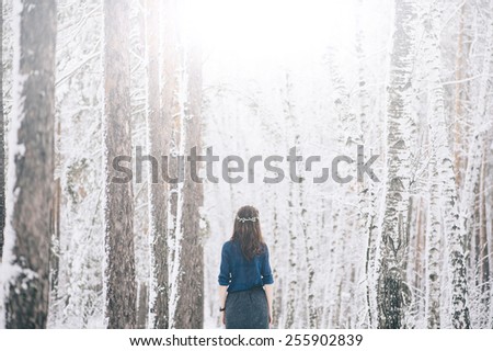 Beautiful attractive woman standing back to the camera in the snowy winter forest