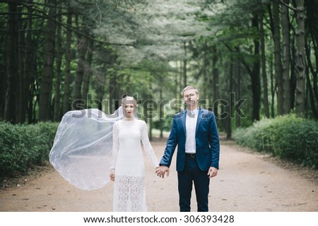 Beautiful married young couple standing with brides veil waving in the wind in the forest all alone