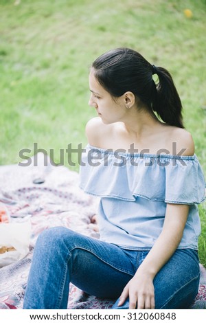 Beautiful brunette with a pony tail having a picnic on a green grass, on a hot summer day