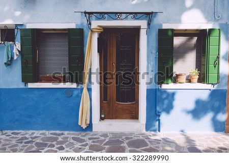 Beautiful house facade on Burano island, north Italy. Colorful blue house wall with a door and some windows