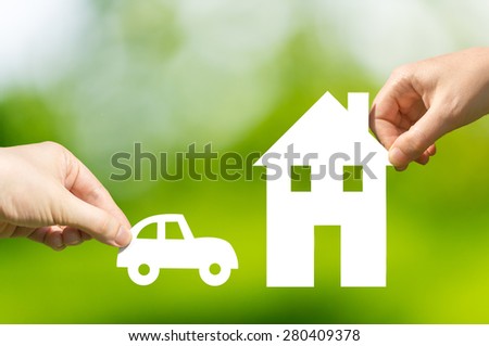 Two hands holding cut out paper car and house