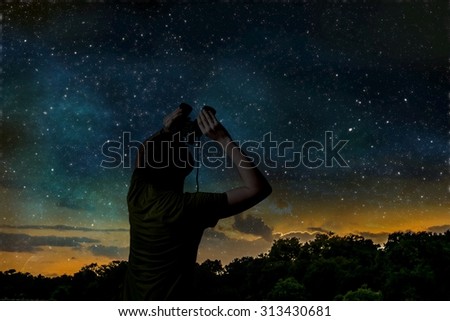 Silhouette of adult man is observing stars on night sky with binoculars.