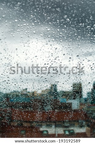 Streaks and drops of rainwater on a windowpane on a dull overcast day, on the background of the city