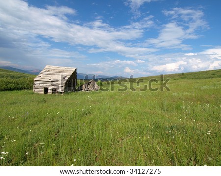 Wide angle view of abandoned wood cabin in green field.