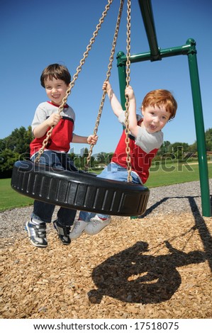 Two brothers have fun swinging on a tire swing at a neighborhood park.
