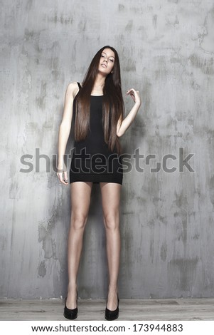 Beautiful woman with long legs. Beautiful woman in full growth. Photo near the wall. Long beautiful legs. Black dress. Long shiny hair.