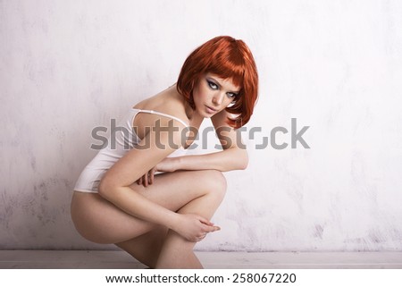 Beautiful girl with red hair on a white background sits in a pose. Beautiful young woman. White background. Sit down on one knee