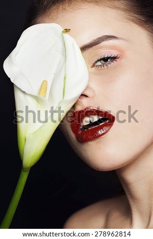 Beautiful young woman with white flower professional make up. Perfect skin. Fashion model. Black background. Portrait close up. Red lips.