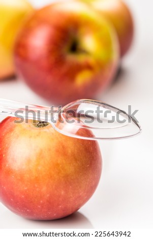 red apple and translucent medicine spoon on the table symbolizing that drinking and eating of apple products prevents diseases and is full of vitamins, other apples at background
