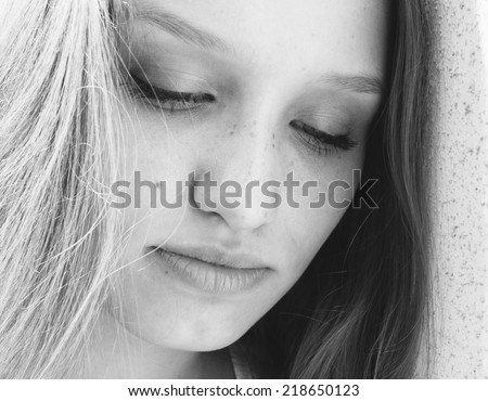 Beautiful young woman with downcast eyes and a serious serene expression, close up greyscale face portrait