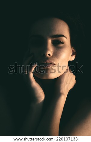 Dark portrait of a beautiful mysterious sexy young woman with her hands to her head staring dreamily at the camera