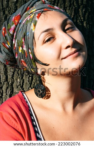 Pretty Smiling Young Woman with head Cover Leaning on Tree
