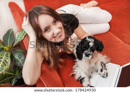 Caucasian girl is resting with dog and laptop on the sofa. Indoor.