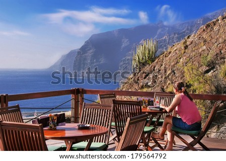 Tenerife island, Canary, Spain - March 30, 2013. Caucasian girl is resting in the cafe in front of Los Gigantes cliffs. Young woman is enjoying view  of serene ocean.