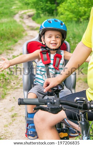 Protection on the bicycle. Caucasian joyful happy child have biking helmet. The little cute  boy is in the bicycle chair (seat) during bicycle ride. Summer travel concept. Close up.