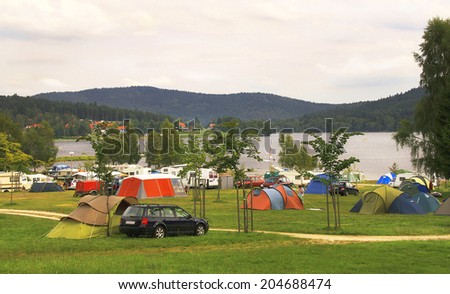 Lipno, Czech Republic - August 12, 2010. Camping tent with cars and caravan trailers (vans) in the meadow among mountains by lake. It is a popular place for relax. Travel concept.