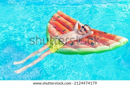 Happy nine years old child (boy) in red sunglasses lying on the inflatable ring (air mattress) in swimming pool. Kid water toys, safety on the water, learning to swim. Family beach vacation. Summer.
 Foto stock © 