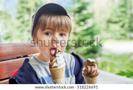 Ice cream cone - yummy! Cute boy with two delicious ice cream on green background. Little child (toddler, kid) eating tasty ice-cream. Caucasian male model. Food, summer, travel concept. Copy space.