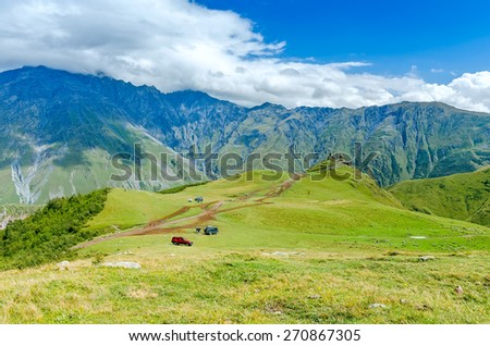 View on road to small church in mountains with beautiful clouds. The cars and stones on the way