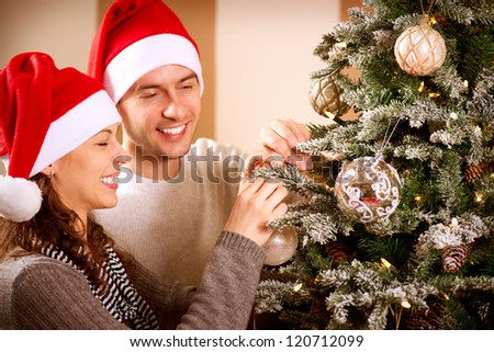 Happy Couple Decorating Christmas Tree in their Home. Smiling Man and Woman together Celebrating Christmas or New Year. Christmas Tree Decoration.Family