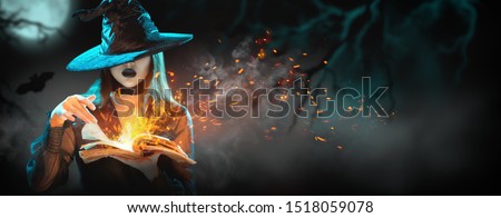 Halloween Witch girl with magic Book of spells portrait. Beautiful young woman in witches hat conjuring, making witchcraft. Over spooky dark magic forest background. Wide Halloween party art design.