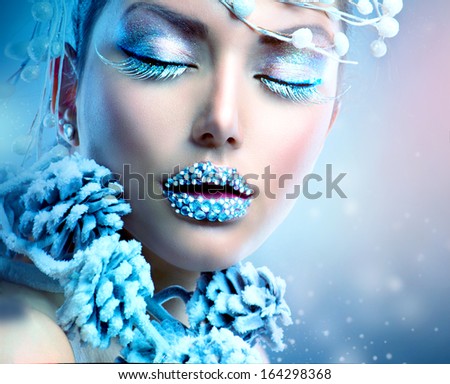 Winter Beauty Woman. Christmas Girl Makeup. Holiday Make-up. Snow Queen High Fashion Portrait over Blue Snow Background. Eyeshadows, False Eyelashes and Crystals on the Lips. Copy Space for Your Text