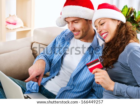 Online Christmas Shopping. Happy Smiling Couple Using Credit Card to Internet Shop. Young Family with laptop and credit card buying online. Christmas and New Year Gifts. e-shopping