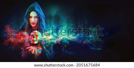 Halloween Witch woman holding human skull lantern in her hands. Beautiful young girl. Darkness. Scary backdrop. Over spooky dark magic background. Magic concept. Art design