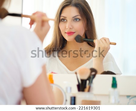 Beauty woman applying makeup. Beautiful girl looking in the mirror and applying cosmetic with a big brush. Girl gets blush on the cheekbones. Powder, rouge