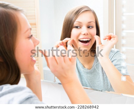 Beauty young woman flossing her teeth at home. Pretty teenage girl using an interdental brush smiling at the mirror enjoying beautiful white teeth. Healthcare of mouth and dental floss. Dental hygiene
