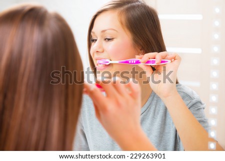 Beauty teenage girl brushing her teeth at home. Pretty young woman using a toothbrush, smiling at the mirror, enjoying beautiful white teeth. Healthcare of mouth, dental hygiene