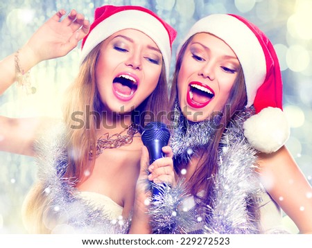 Christmas party, karaoke. Beauty girls in santa hat with a microphone singing and dancing over holiday blinking background. Disco. New year celebration