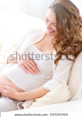 Pregnant Happy smiling Woman sitting on a sofa and caressing her belly. Mom Expecting Baby. Pregnant Woman Belly. Pregnancy. Beautiful Pregnant Woman. Maternity concept. Baby Shower