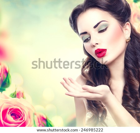 Retro woman portrait in beauty pink roses garden. Beautiful Vintage styled girl with flowers. Perfect makeup and hairstyle. Gorgeous model lady. Red Lips. Luxury Make up and Hair. Vogue Style