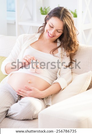 Pregnant Happy Woman holding Baby Shoes in her Hands. Mom Expecting Baby. Pregnant Woman Belly. Pregnancy. Baby Shower