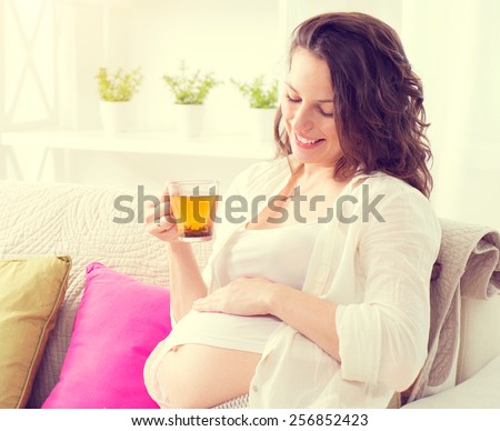 Pregnant Happy smiling Woman sitting on a sofa and drinking herbal tea. Mom Expecting Baby. Pregnant Woman Belly. Pregnancy. Beautiful Pregnant Woman. Maternity concept.