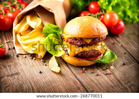 Hamburger with fries on wooden table. Cheeseburger on fresh buns with succulent beef patties and fresh salad ingredients served with French Fries on a wooden table