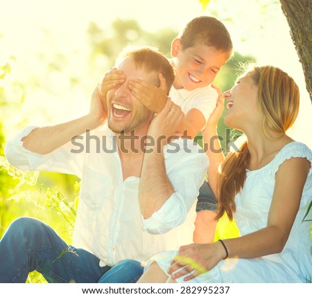 Happy joyful young family father, mother and little son having fun outdoors, playing together in summer park. Mom, Dad and kid laughing and hugging, enjoying nature outside. Sunny day, good mood