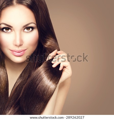 Beauty Model girl with Healthy Brown Hair. Beautiful brunette woman touching her long smooth shiny straight hair. Hairstyle. Hair cosmetics, haircare. Hair care, extensions. Brown background
